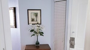 A hallway with a wooden dresser, a framed picture, a door with a window, and a patterned rug.