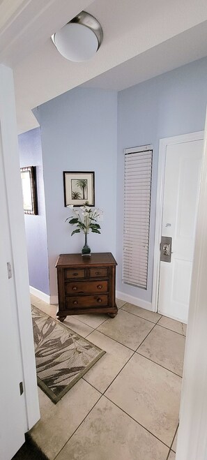 A hallway with a wooden dresser, a framed picture, a door with a window, and a patterned rug.