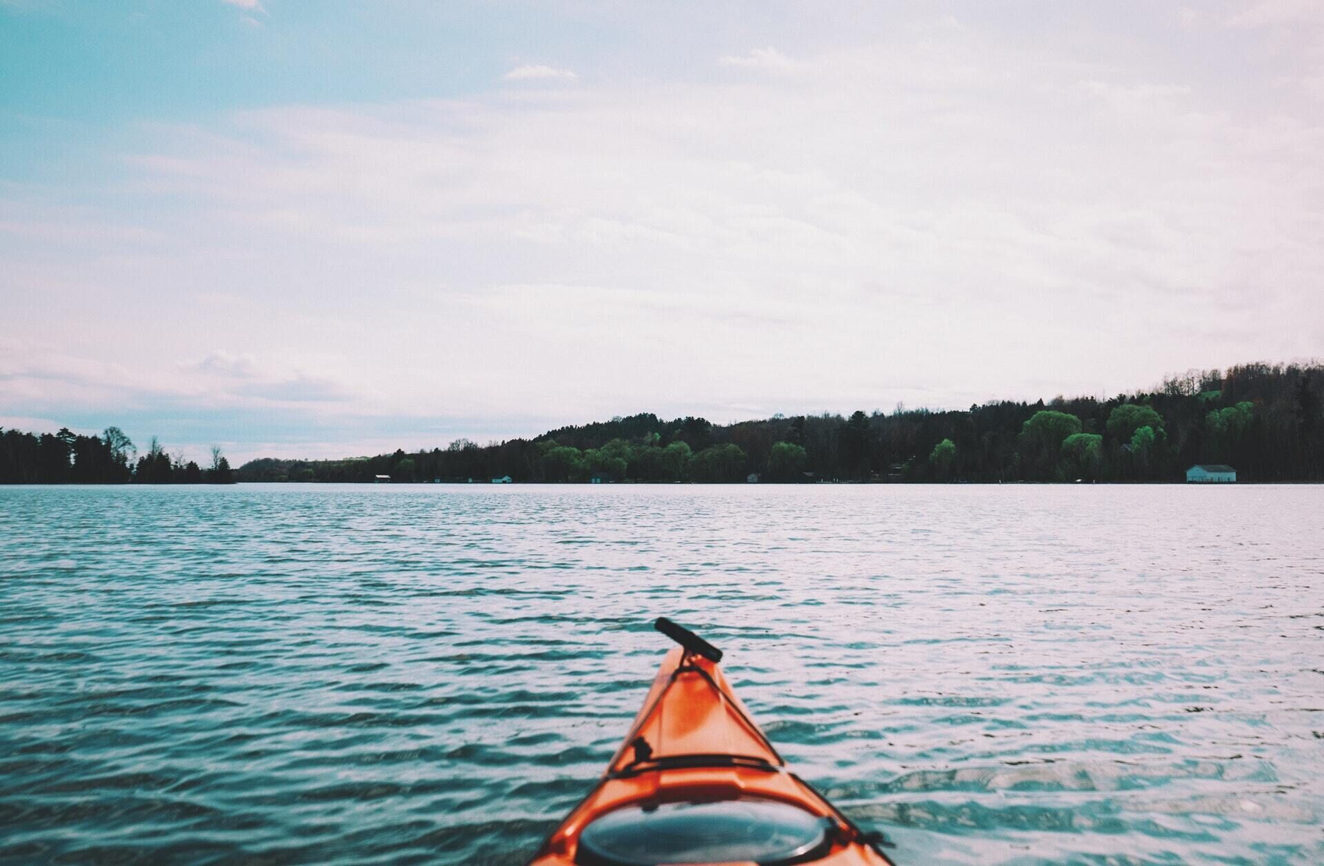 A kayak on calm water with a forested shoreline in the background.