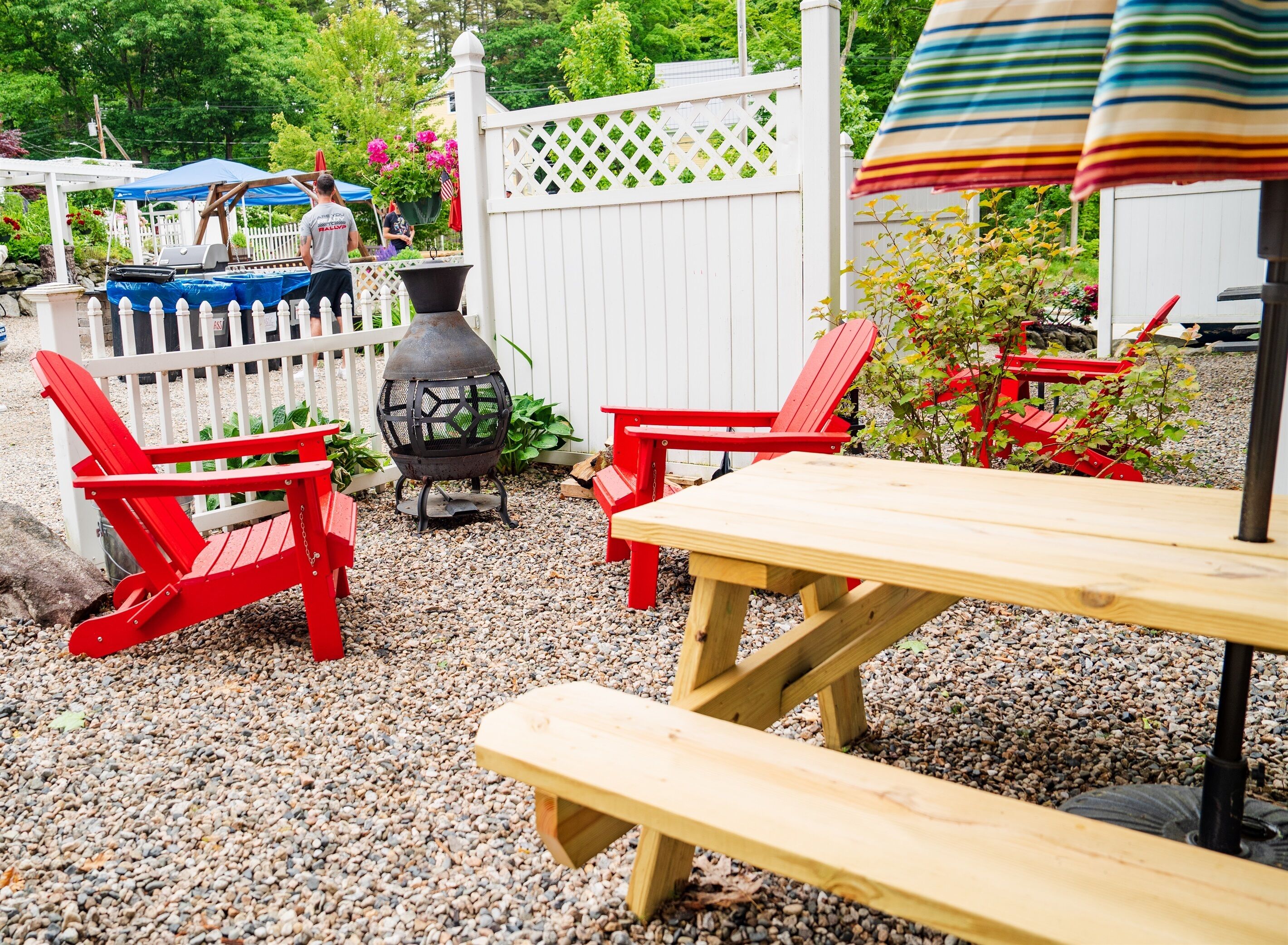 A patio area with red Adirondack chairs, a wooden table, and a grill.