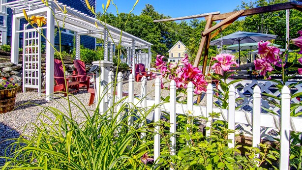 Een tuin met een witte pergola, rode stoelen en roze bloemen.