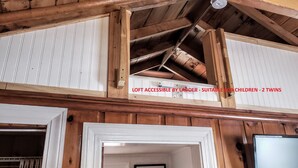 Een slaapkamer in een loft met houten plafond en witte wanden. Toegankelijk via een ladder, geschikt voor kinderen.