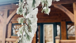 Una cabaña de madera con un porche cubierto de nieve y ramas de pino.