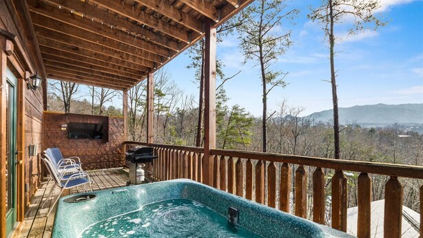 Un jacuzzi en una terraza de madera con vista a árboles y montañas.