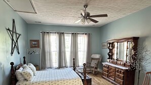 Ein Schlafzimmer mit einem hölzernen Bett, einem Schminktisch, einem Schaukelstuhl und einem Deckenventilator.