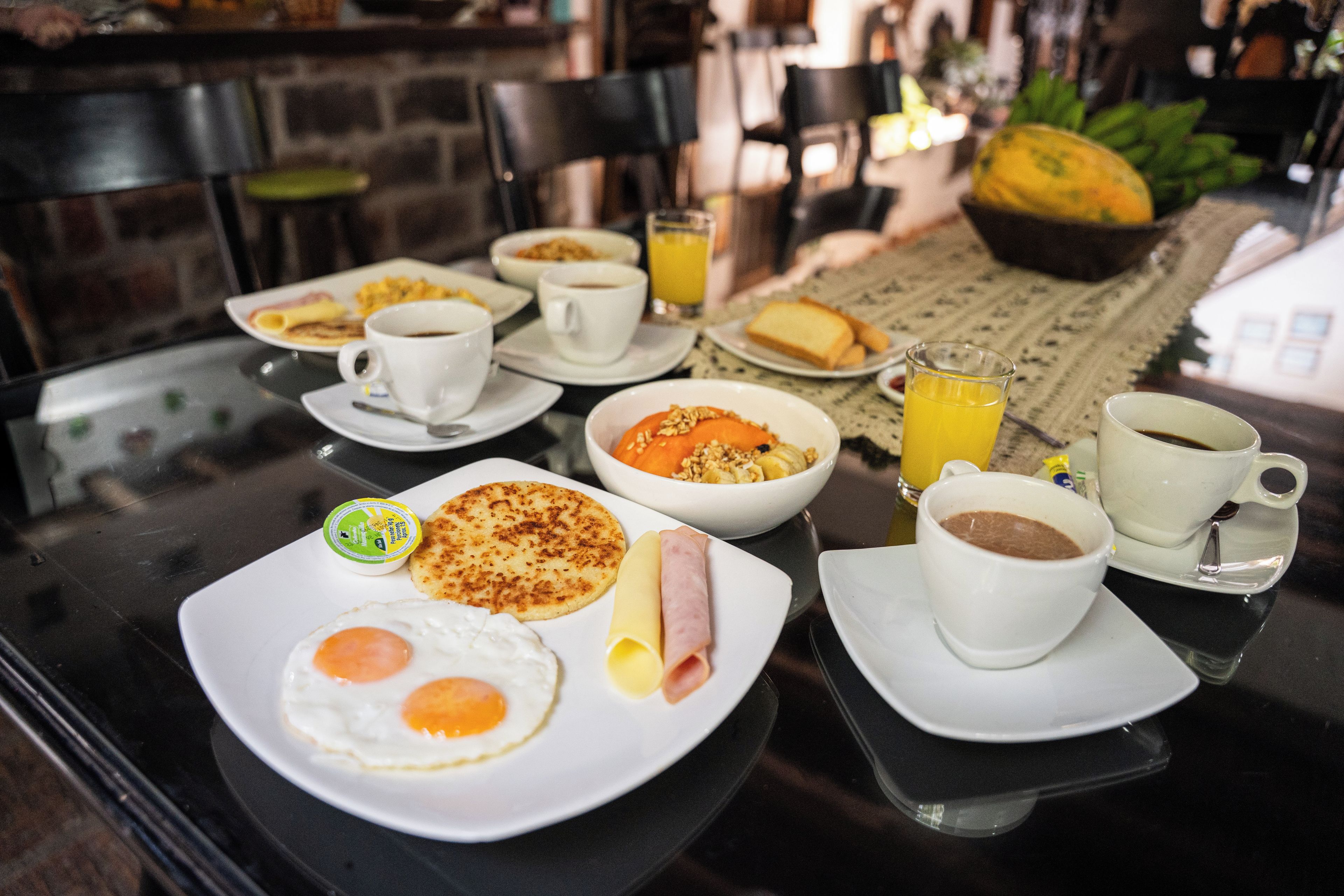 Una mesa de desayuno con platos de comida, tazas y un vaso de jugo de naranja.
