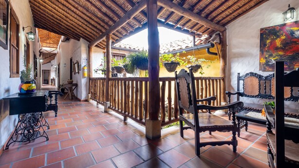 A covered patio with terracotta tiles, wooden furniture, and hanging plants.