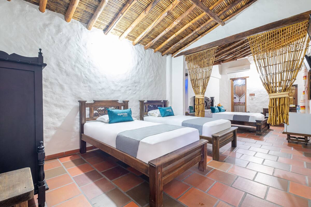 A room with two beds, a wooden bench, a wardrobe, and a bamboo curtain.