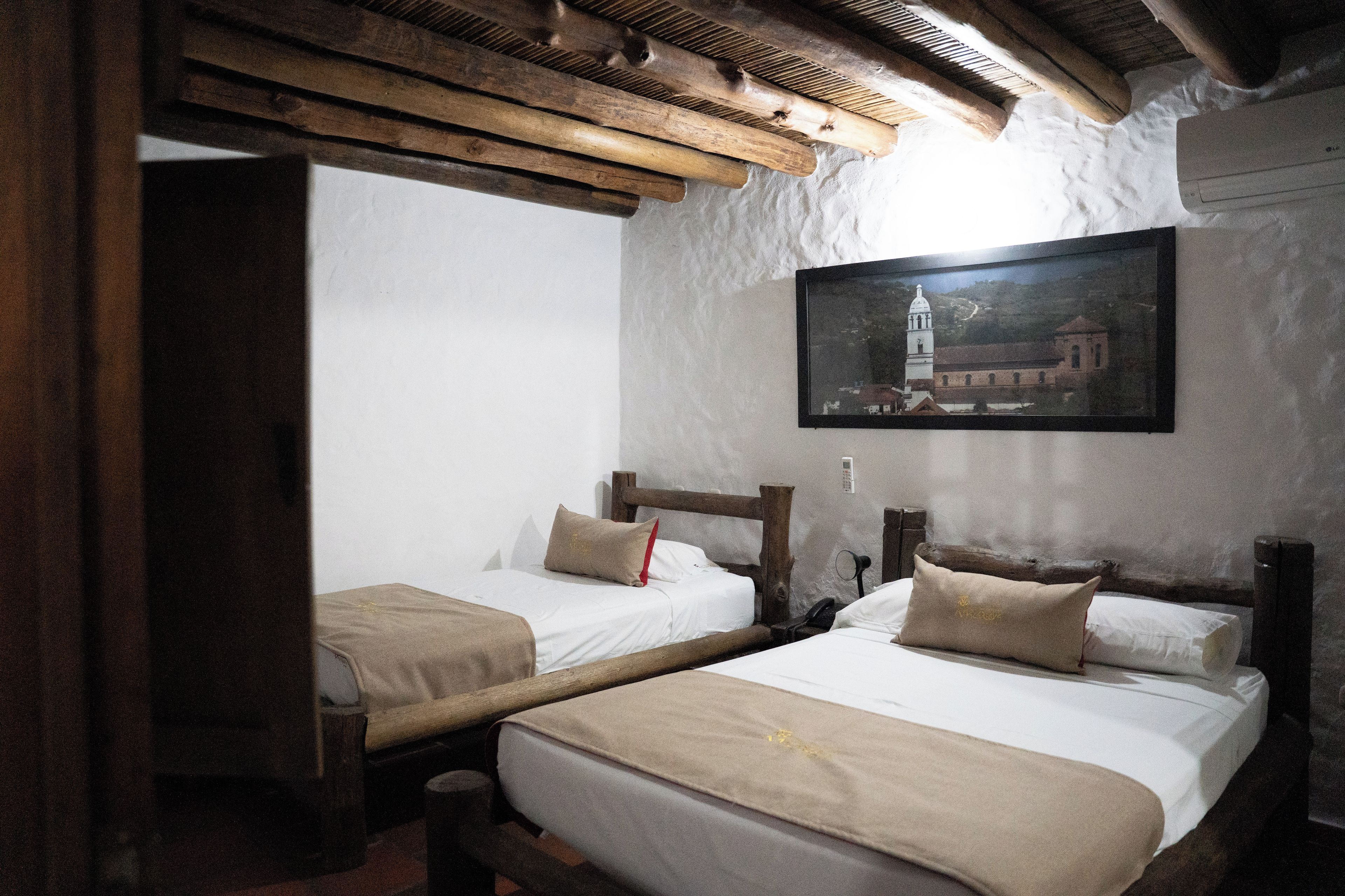 A room with two wooden beds, a painting on the wall, and a wooden ceiling structure.