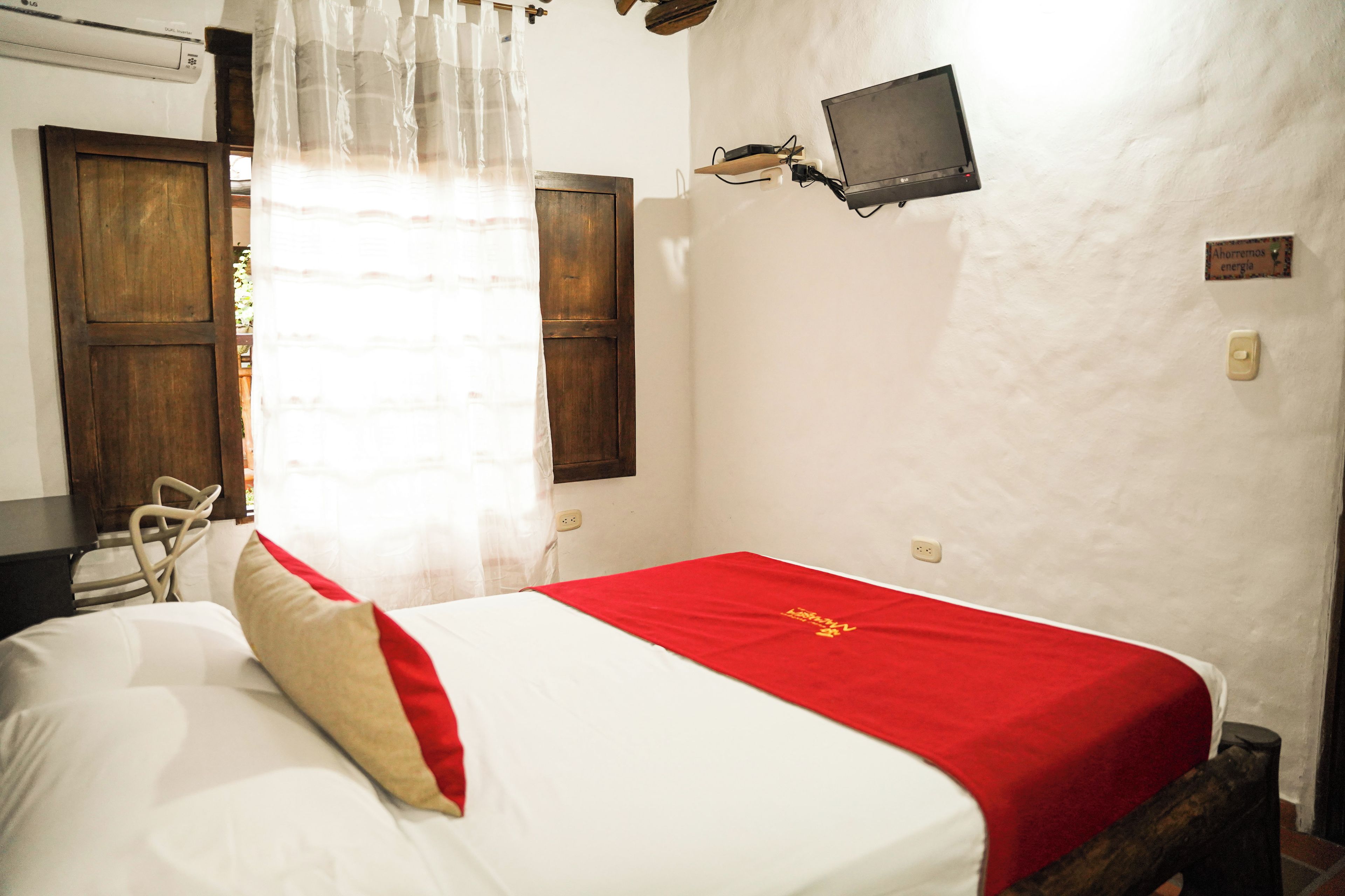 A room with a bed, a wall-mounted TV, and a window with curtains.