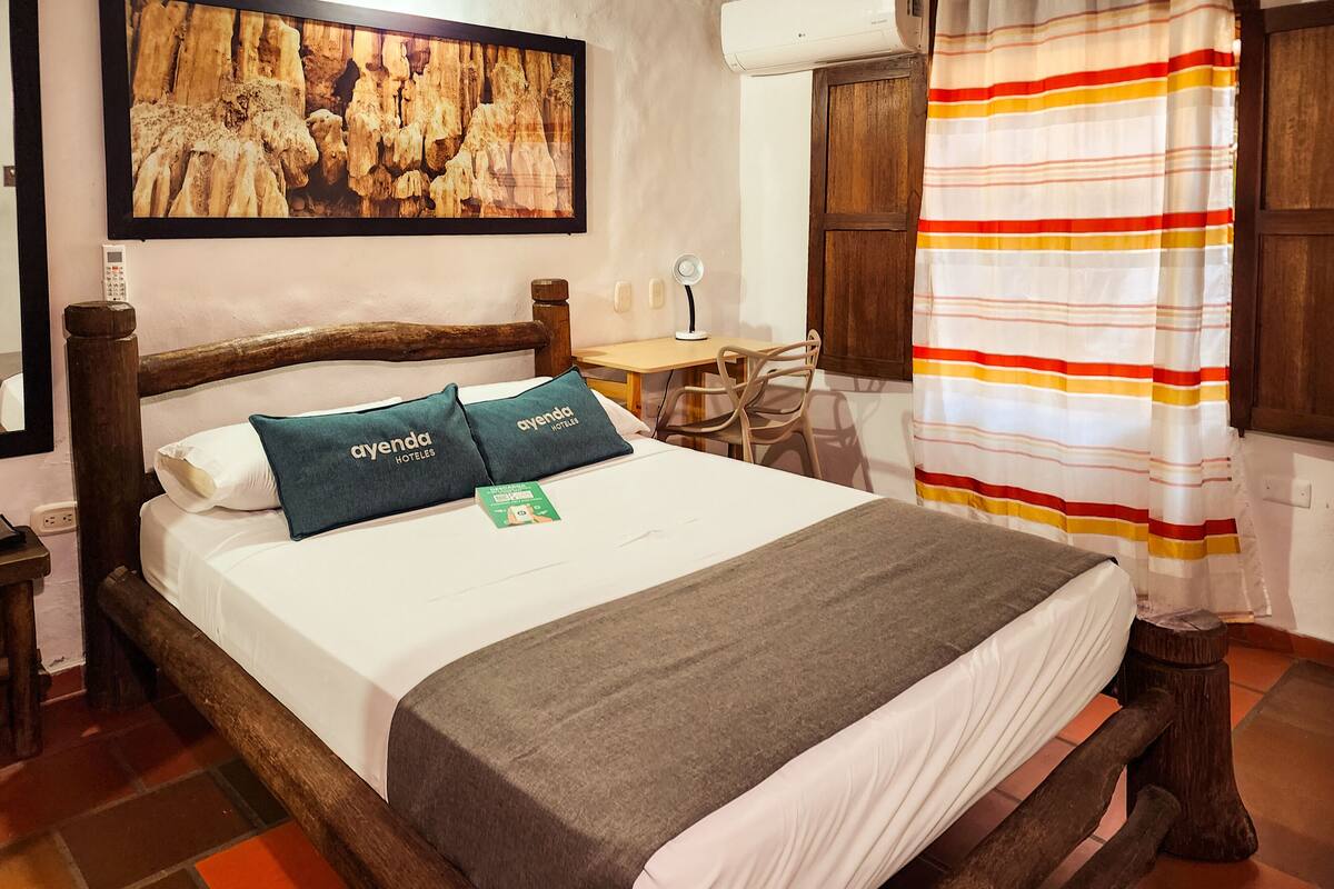A wooden bed with two pillows, a bedside table, a desk, and a chair.