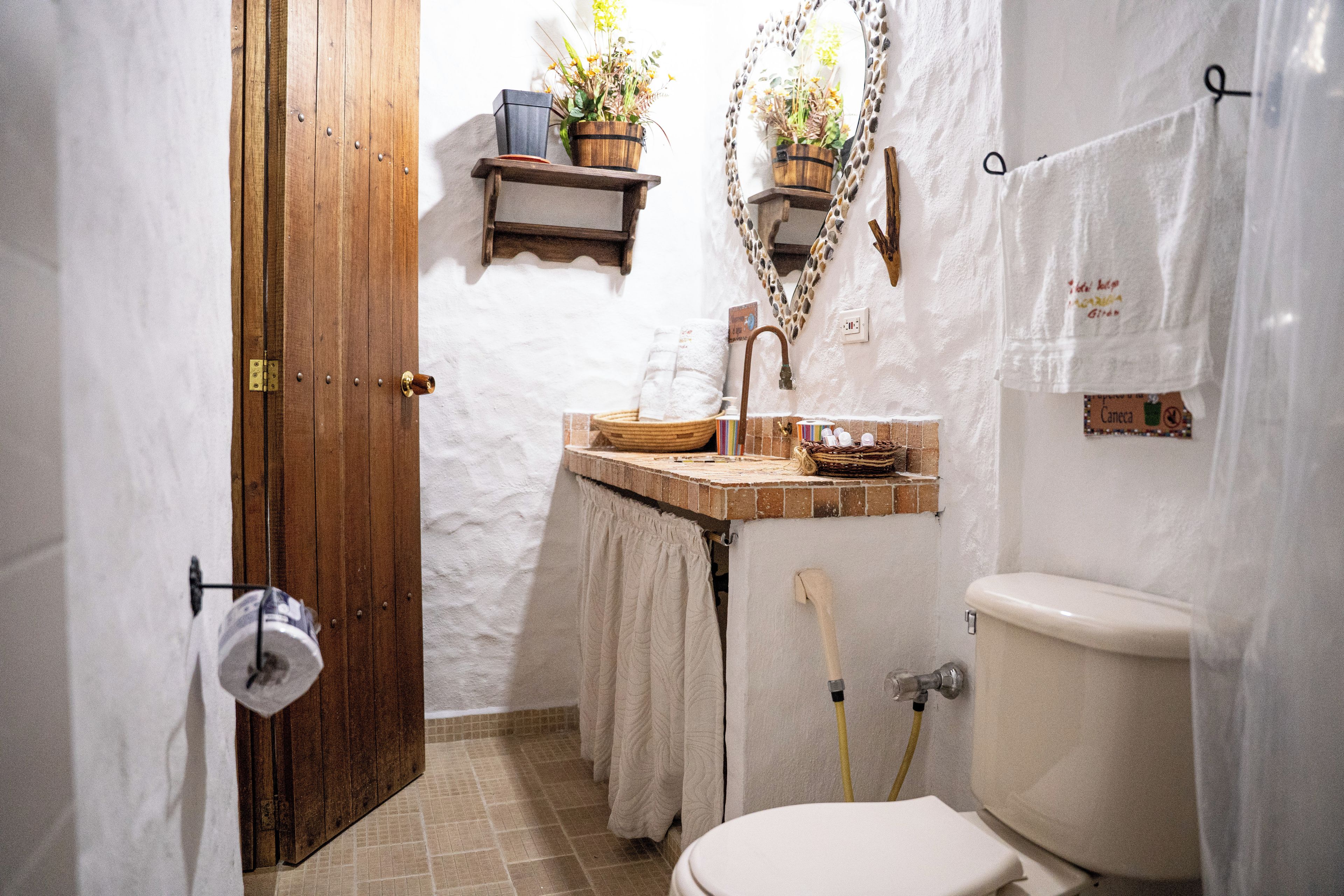 Un baño con puerta de madera, inodoro, lavamanos con espejo y un perchero para toallas.