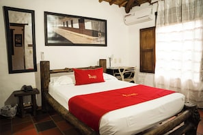 Een hotelkamer met een bed, nachtkastje, telefoon, een luchtverkoeler aan de muur en een raam met gordijnen.