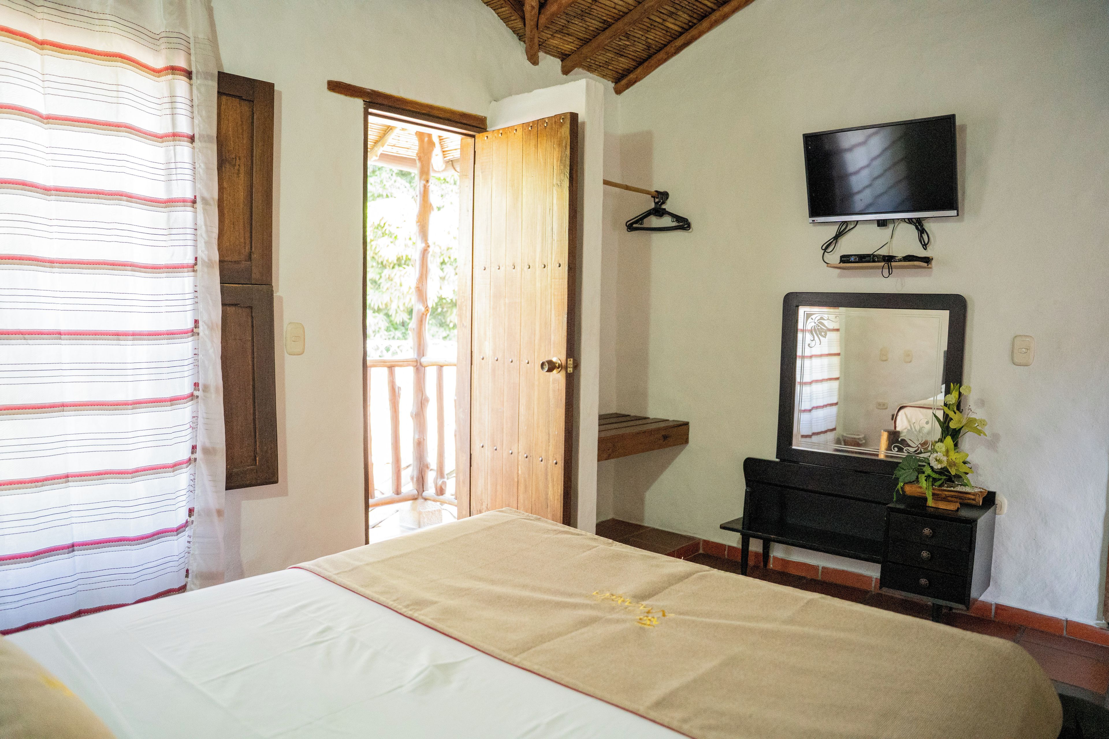 Un dormitorio con cama, cómoda, espejo, televisión y puerta que da a un área exterior.
