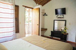 A bedroom with a bed, a dresser, a mirror, a television, and a door leading to an outdoor area. - Hotel Boutique Macaregua Giron (Giron)