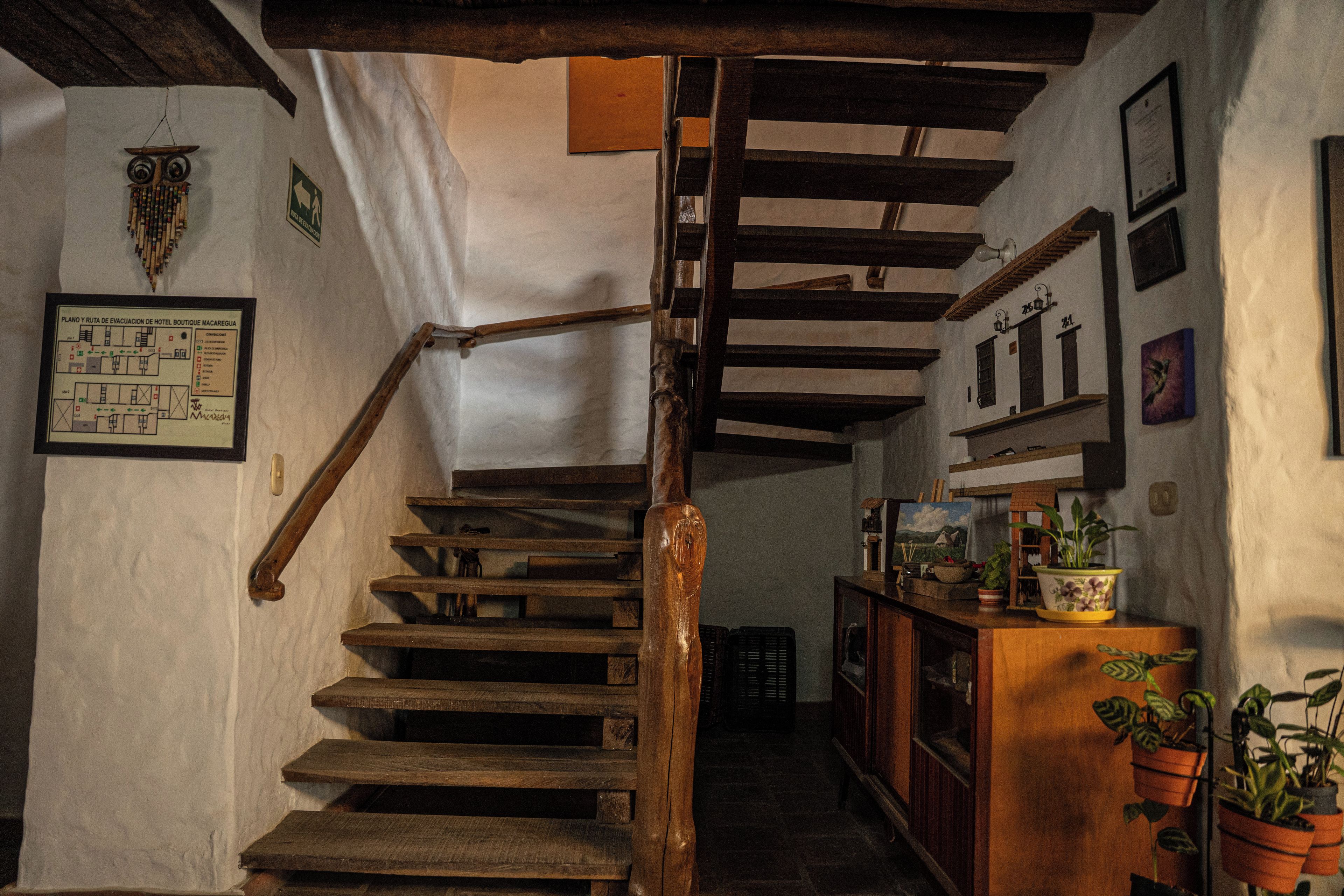 A wooden staircase with a handrail leading to a landing. There are framed pictures and a map on the walls.