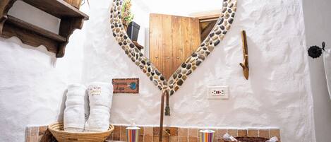 Un baño con un espejo con forma de corazón, toallas, un dispensador de jabón y un lavamanos pequeño.