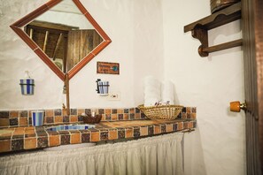 Een badkamer met een betegeld wastafelblad, een spiegel, een handdoekrek en een mand.