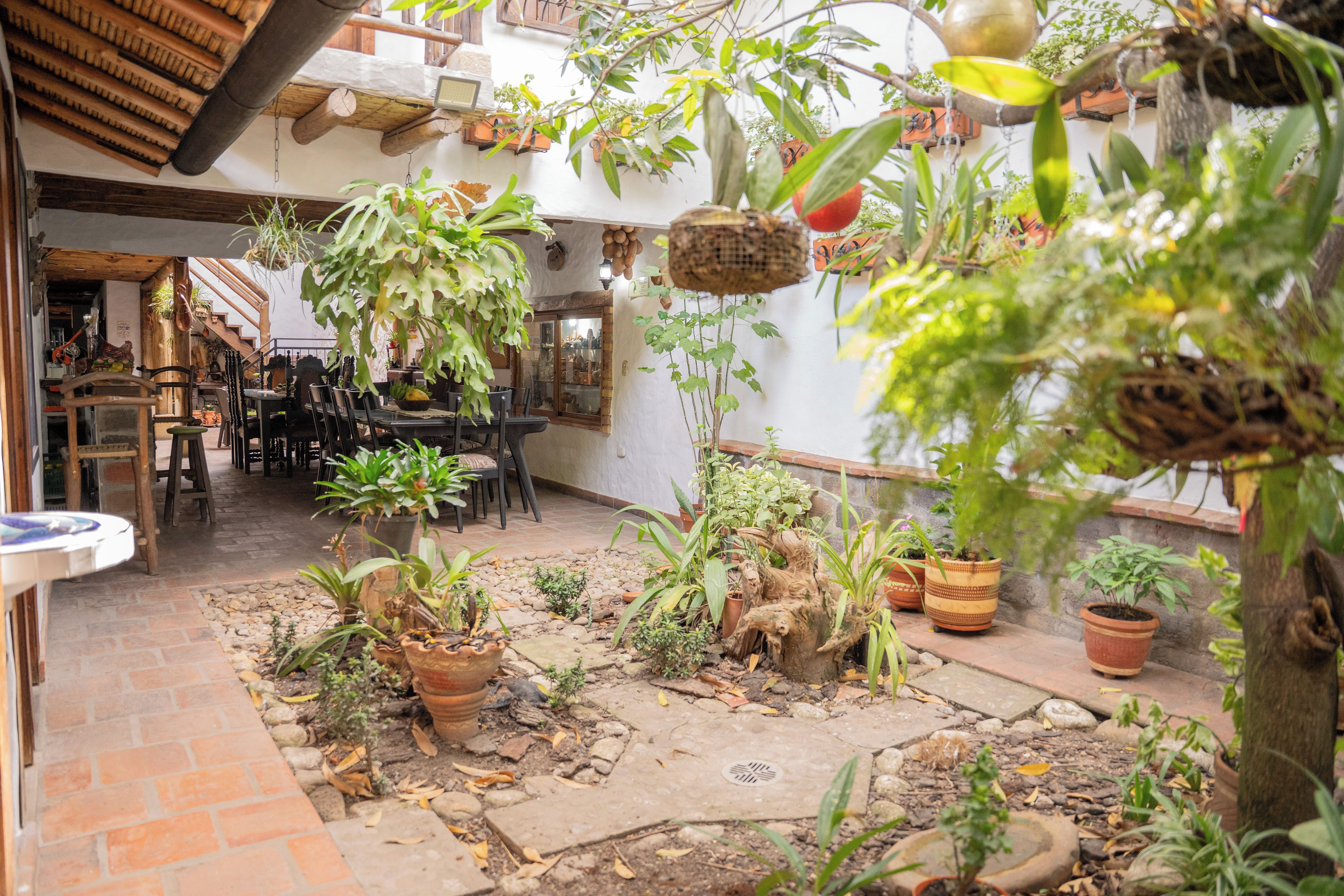 An outdoor patio area with potted plants, a brick floor, and a wooden table with chairs.