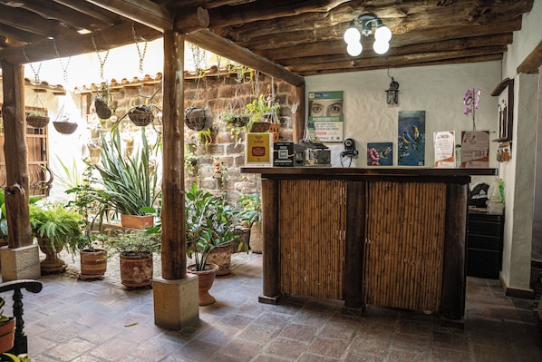 A rustic interior with a wooden reception desk, hanging plants, and a stone wall.