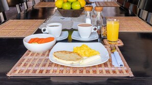 A breakfast setting with a plate of scrambled eggs, toast, and orange juice, along with a bowl of fruit and coffee cups on a table.