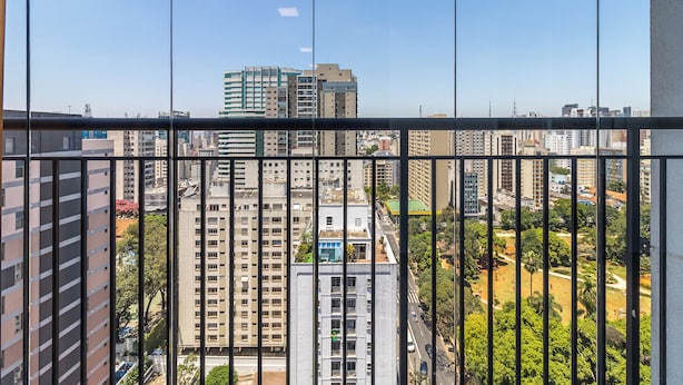 A high-rise building with multiple floors, large windows, and a view of a cityscape through a window with vertical blinds. - Akile Central Park (São Paulo)
