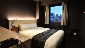 A hotel room with a bed, a desk, a telephone, a window with curtains, and a city view. - FL Hotel Dotonbori (Osaka)