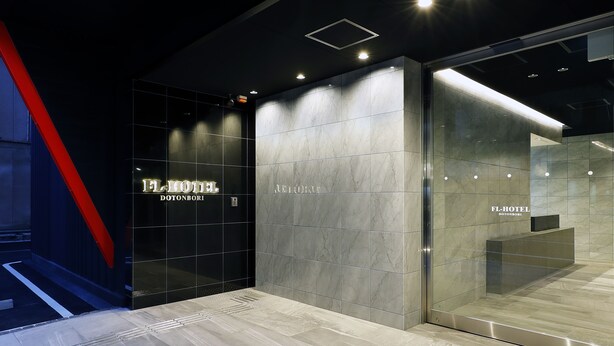 A modern hotel entrance with a glass facade, marble walls, and a prominent red accent on the left. - FL Hotel Dotonbori (Osaka)