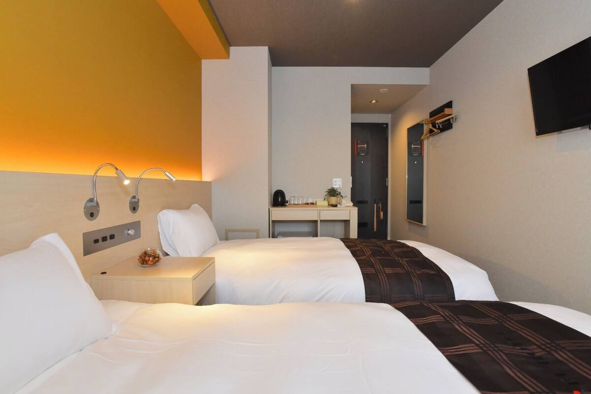 A hotel room with two beds, a desk, a mirror, and a TV.