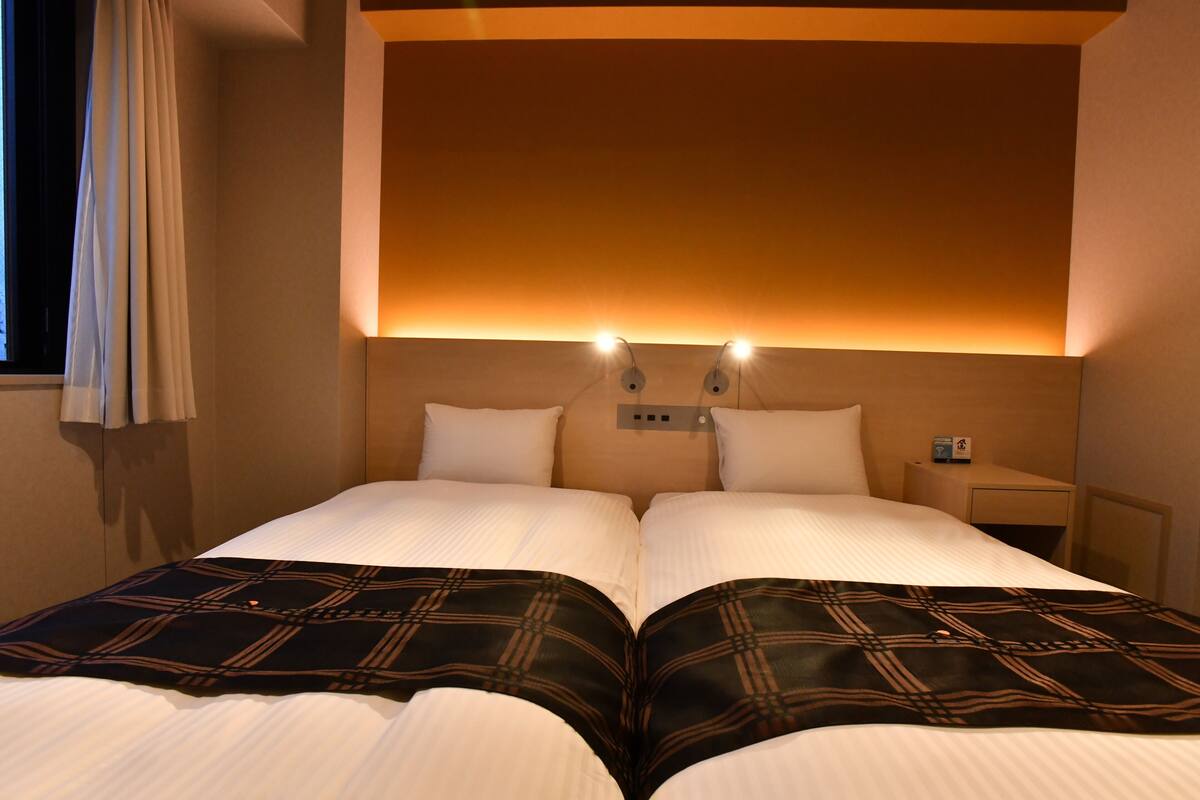 A double bed with a black and brown checkered blanket, two bedside tables, and a wall-mounted light fixture.