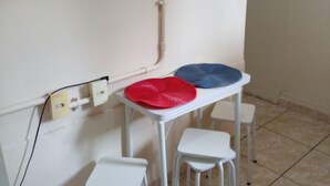 A small dining area with a white table and two chairs, a red and a blue placemat, and a power outlet on the wall. - Privit Studio Brazil (RJ)