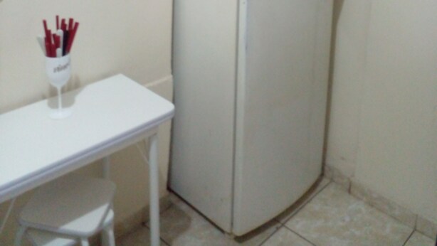 A compact kitchen with a white refrigerator, a small white table, and a cabinet above the fridge. - Privit Studio Brazil (RJ)