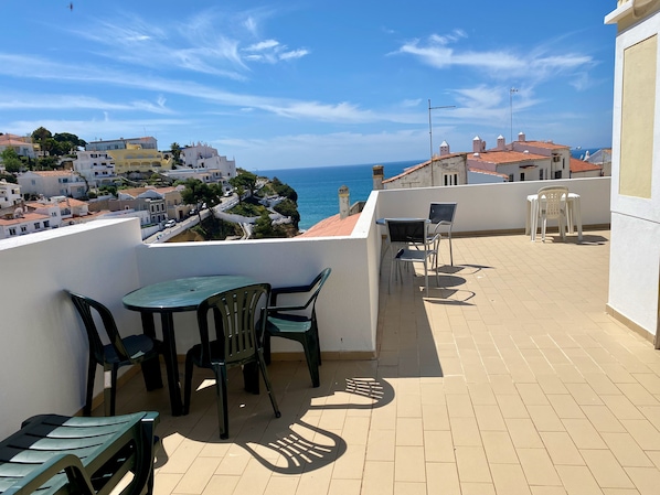 A terrace with a table and chairs, overlooking a coastal town and the sea. - Apartment in Carvoeiro: Wi-Fi, elevator, rooftop terrace, air conditioning, garage. (Carvoeiro)