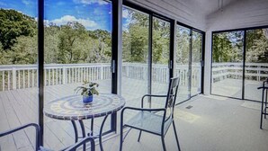 Ein überdachter Außenbereich mit einem runden Tisch und Stühlen, große Fenster mit Blick auf Bäume und Himmel.