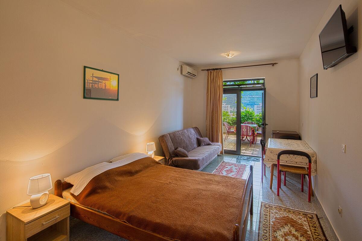 A hotel room with a bed, a sofa, a table with chairs, and a TV mounted on the wall.