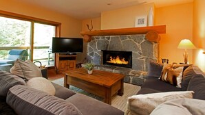 Un salon chaleureux avec une cheminée en pierre, un téléviseur à écran plat et des fauteuils confortables.