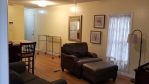 A living room with a brown leather sofa, a small table, and a lamp. There is a door and a window with curtains. - 1/2 acre Private Fenced Dog Friendly (Navarre)