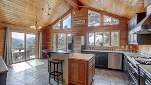 A spacious kitchen with wooden walls, large windows, and a view of the mountains. - Mountain Retreat with Hot Tub Near State Park (Golden)