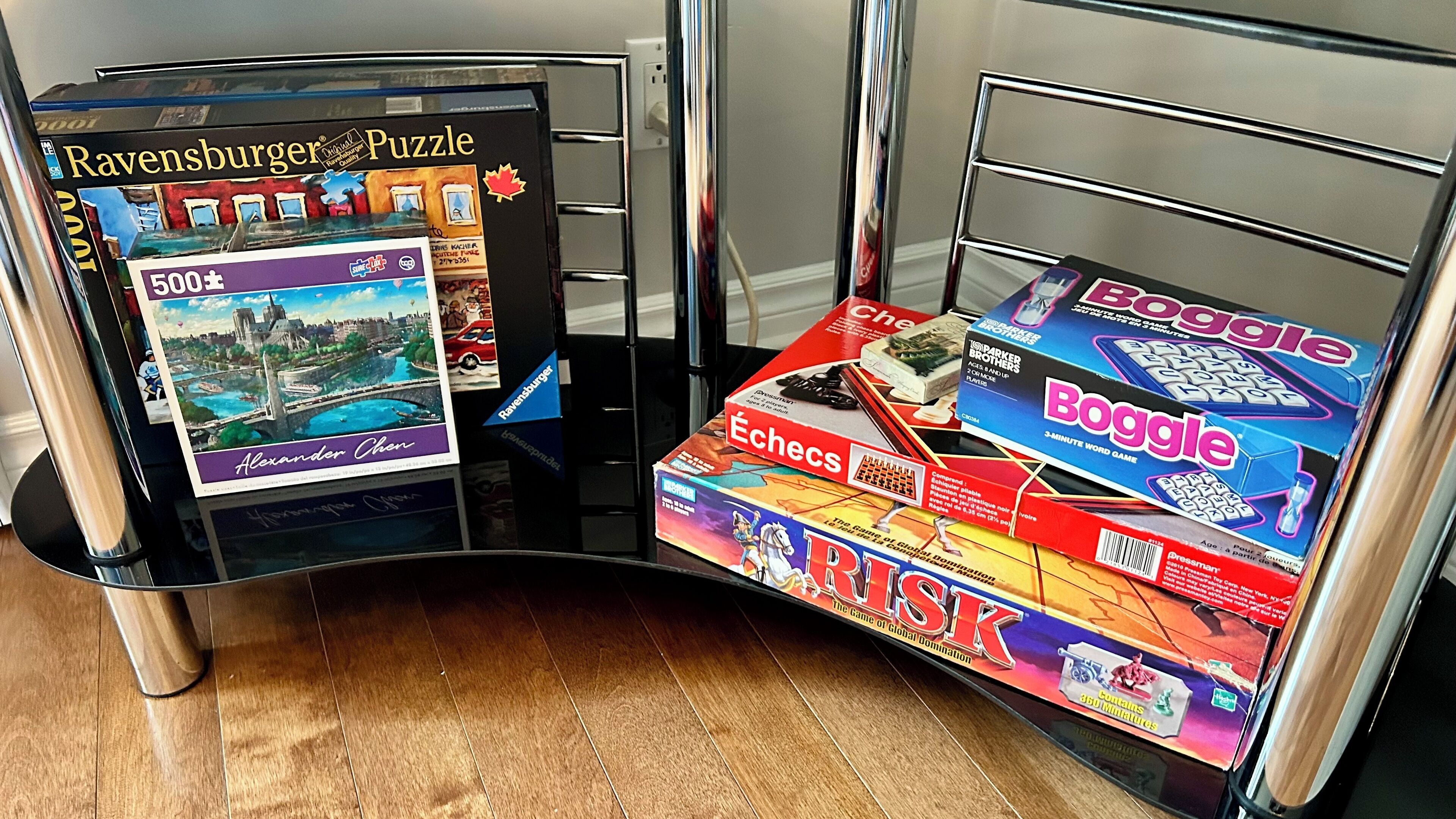 A room with a glass partition, a wooden floor, and various board games like 'Ravensburger Puzzle' and 'Boggle'.