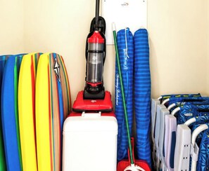 A storage area with surfboards, a vacuum cleaner, and a mop.