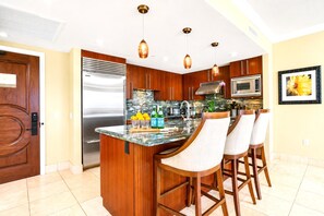 A modern kitchen with a central island, bar stools, wooden cabinets, stainless steel appliances, and pendant lighting.