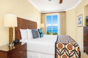 A hotel room with a bed, bedside lamps, a dresser, a window with a view of the ocean, and a ceiling fan.