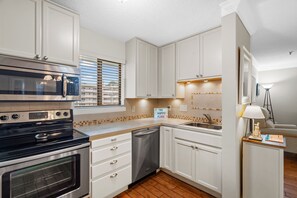 Enjoy cooking in this well-equipped kitchen with stainless steel appliances, white cabinetry, and a tiled backsplash.