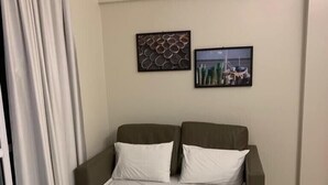 Ein Hotelzimmer mit einem Bett, zwei Kissen, einer weißen Bettdecke, einem Kopfteil, einer Wand mit zwei gerahmten Bildern und einem Fenster mit Vorhängen.