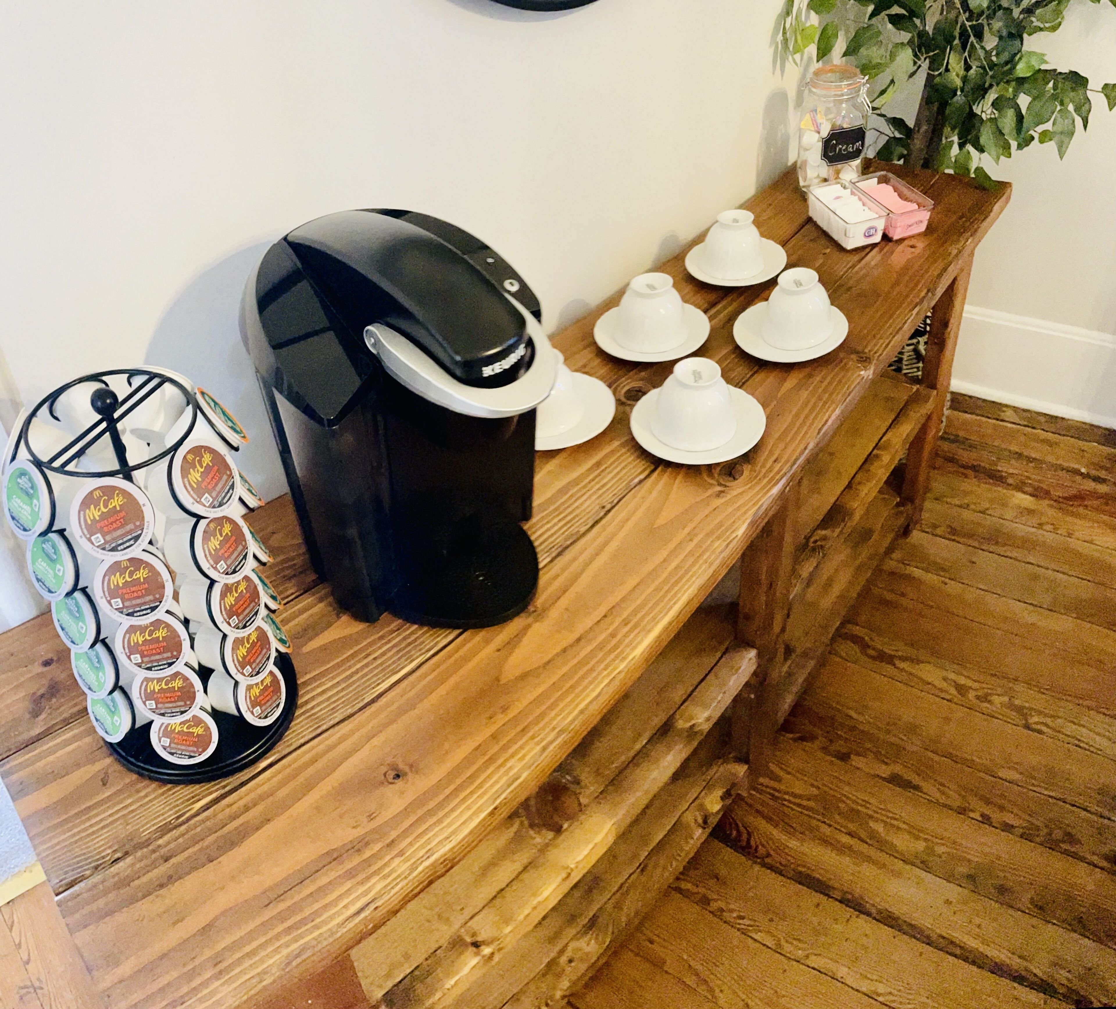 A coffee maker, a McCafe coffee pod holder, and several white teacups on a wooden table.