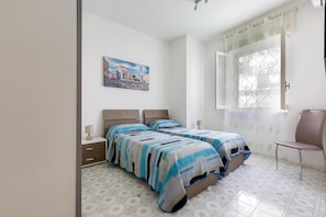 Een slaapkamer met twee bedden, een nachtkastje, een stoel, een raam met gordijnen en een schilderij aan de muur.
