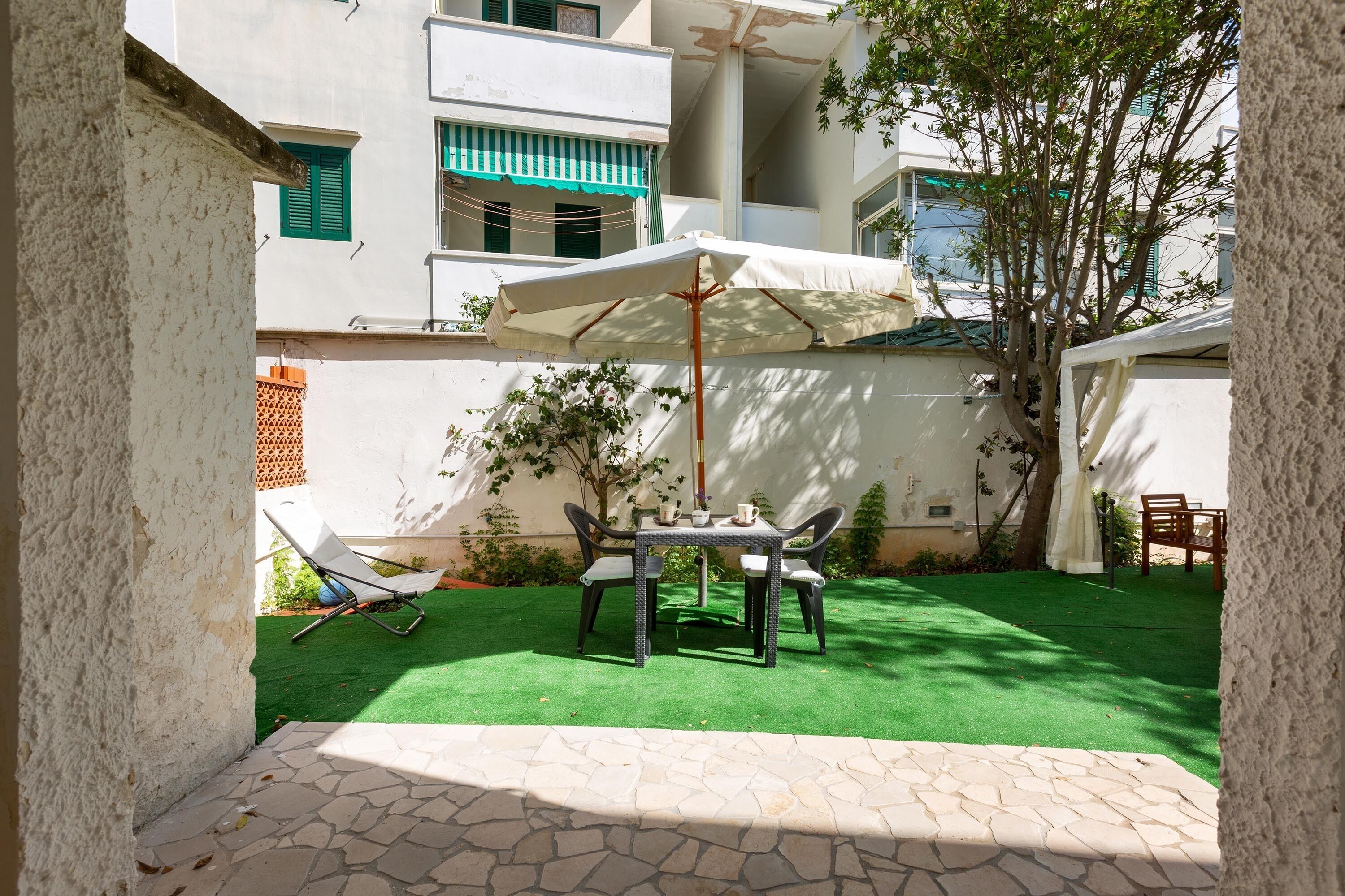 Un patio con tavolo e sedie, un ombrellone bianco e un prato verde.