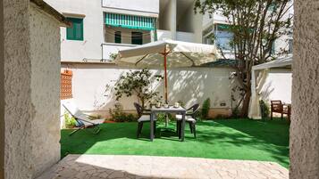 Un patio con tavolo e sedie, un ombrellone bianco e un prato verde.