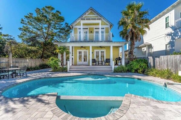 Une maison à deux étages avec un porche à l’avant, une piscine et une clôture en bois.