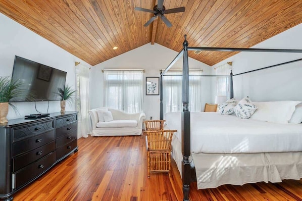 A bedroom with a four-poster bed, a ceiling fan, a TV, and a wooden floor.
